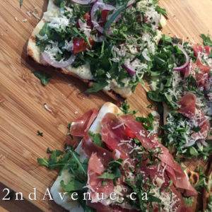 Grilled flatbread topped with arugula, red onion, basil and prosciutto